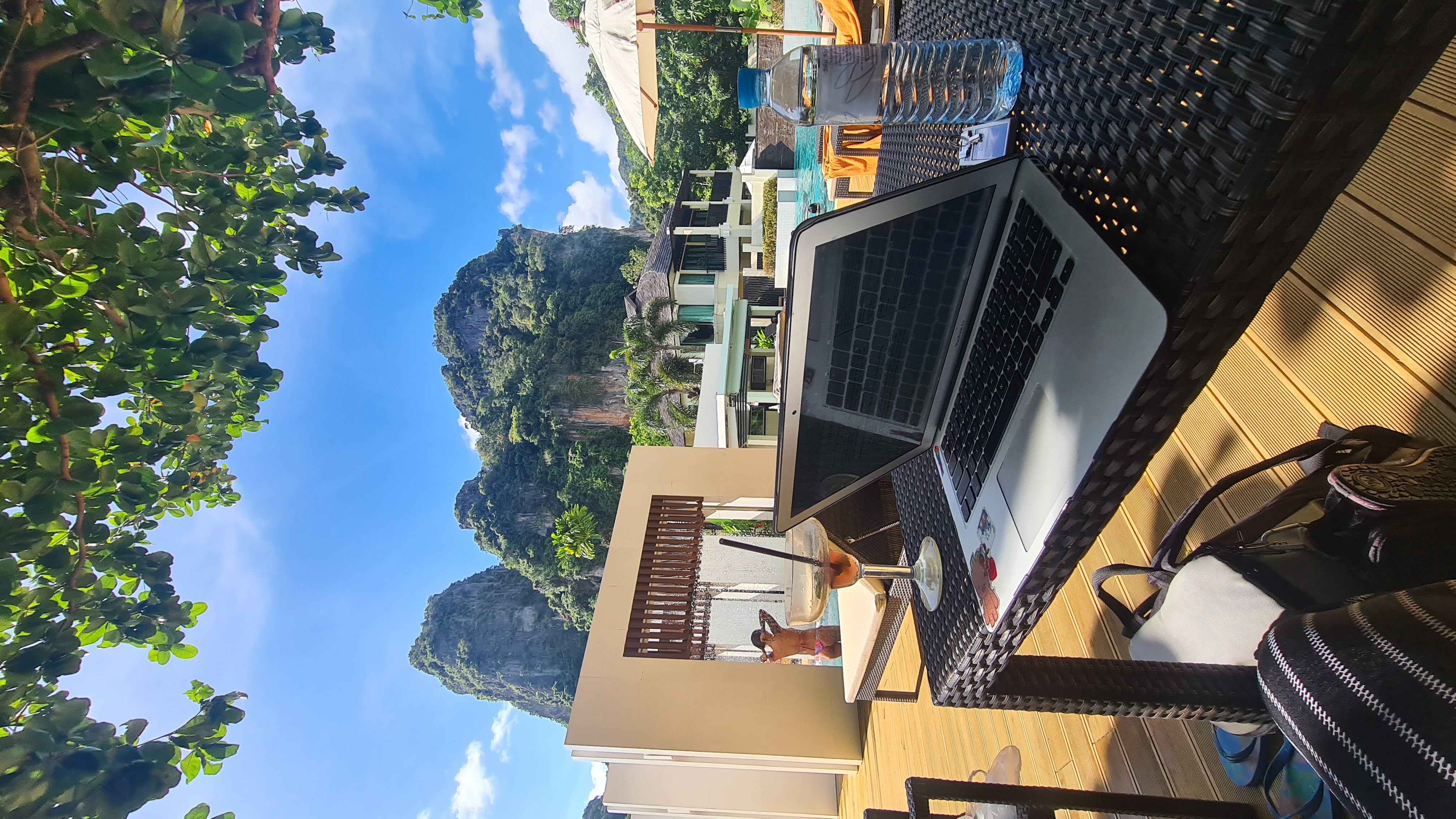 Laptop open beside a pool and limestone cliffs in Thailand