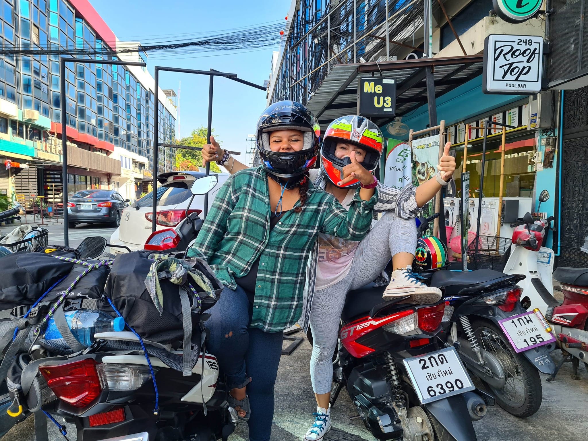 Two women wearing helmets on motorbikes in Chiang Mai before a road trip