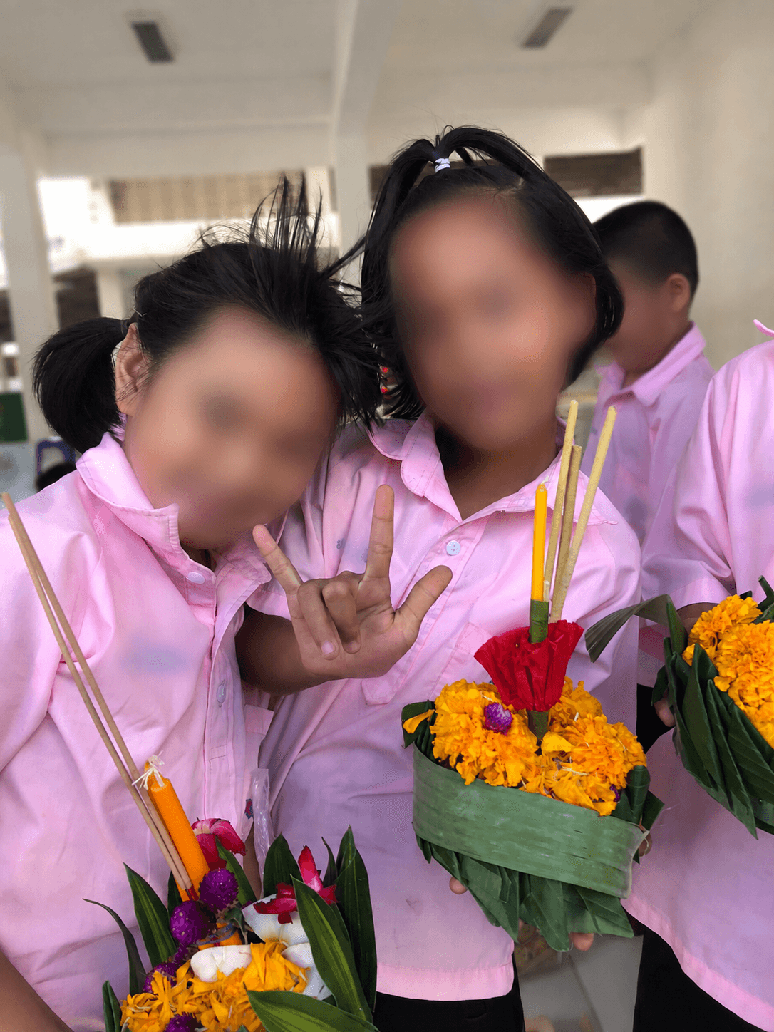 Students holding handmade krathongs with faces and identifying uniform text blurred for privacy