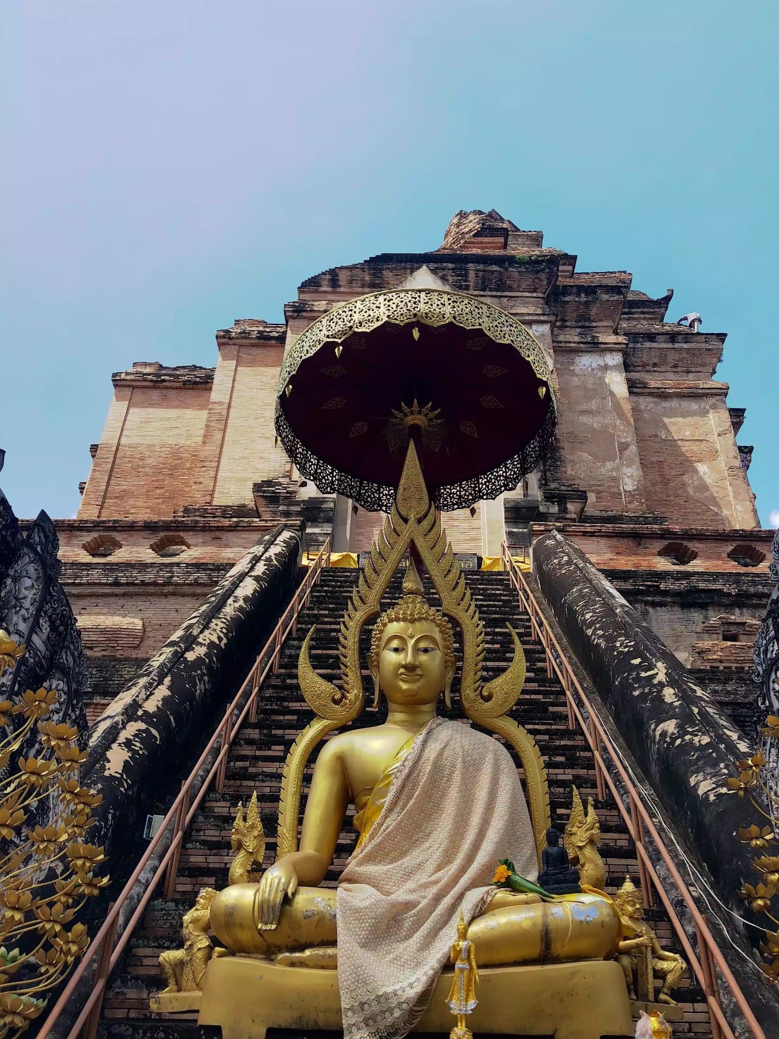 Golden seated Buddha in front of a historic brick chedi in Chiang Mai