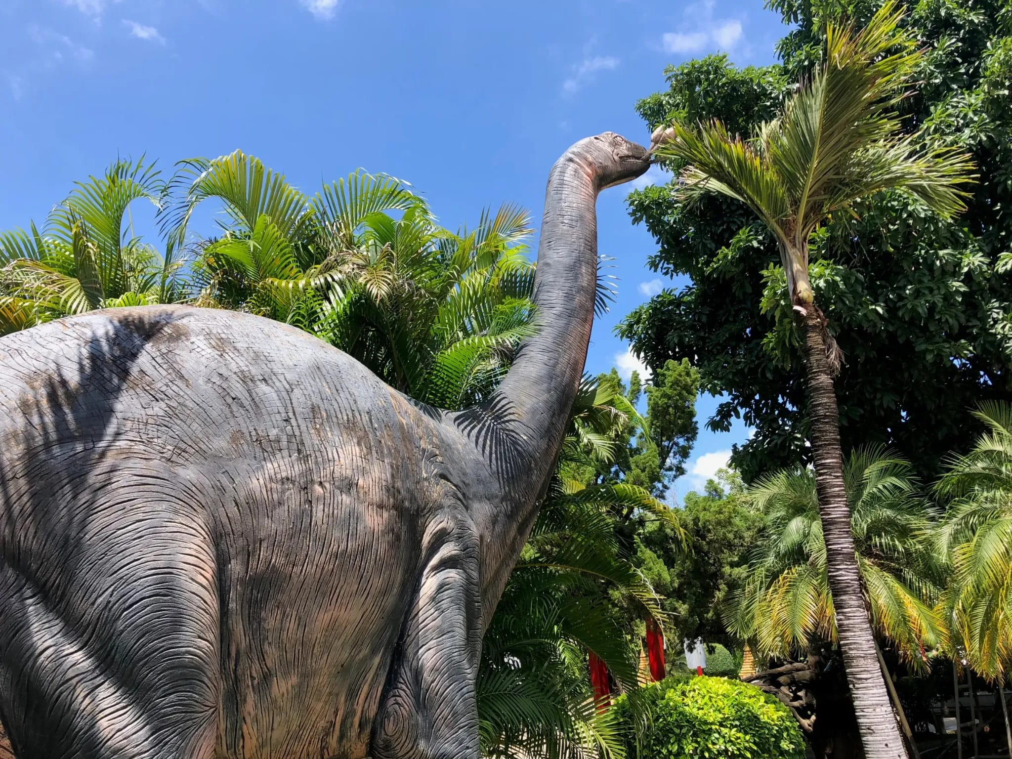Large long-necked dinosaur replica among tropical plants at Wat Nong Waeng in Khon Kaen