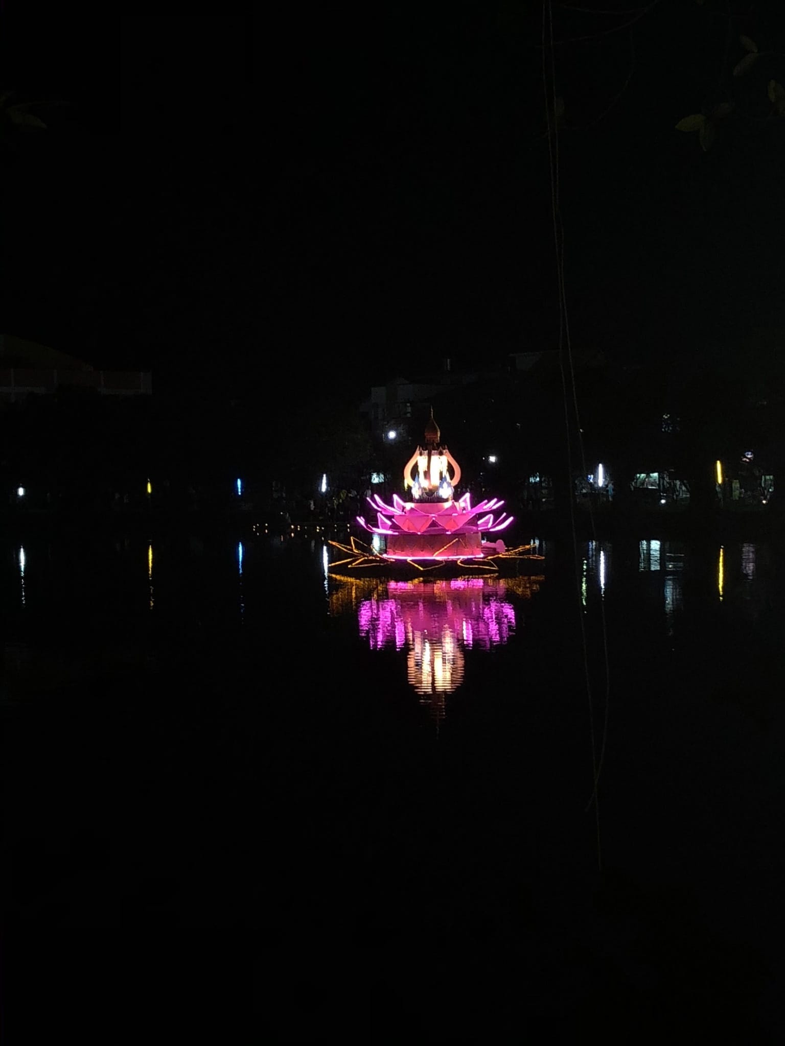 Illuminated floating display reflected in dark water during a Loi Krathong celebration