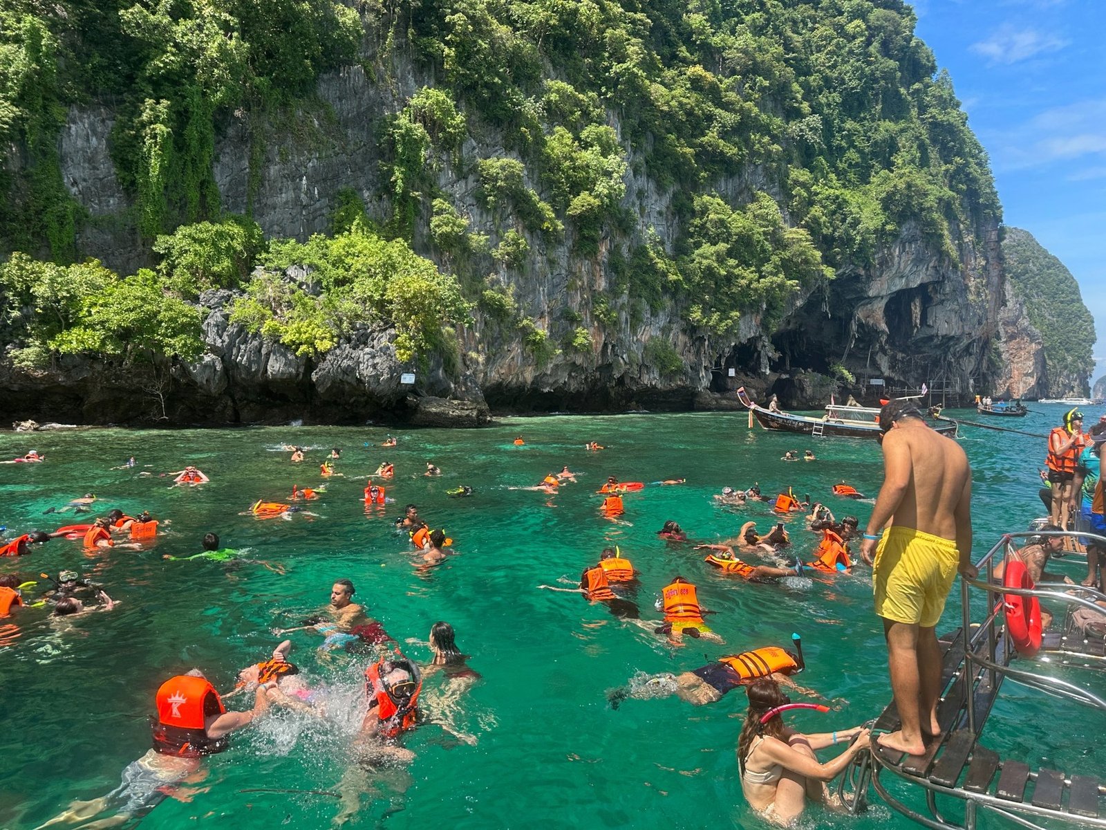 Travelers swimming beside limestone cliffs and longtail boats in southern Thailand